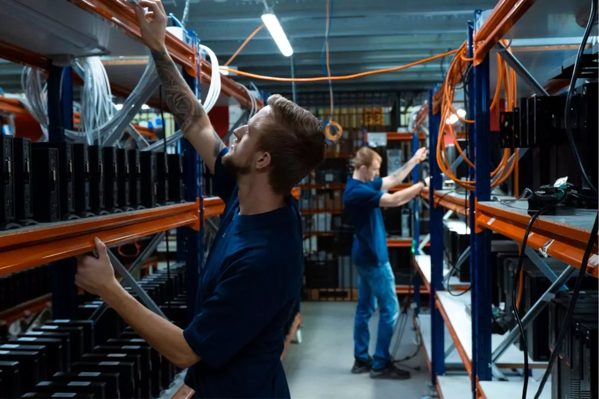 pracownicy rozkładają stary, zużyty sprzęt elektroniczni i IT na regałach w magazynie