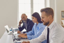 elegancko ubrani ludzie pracują w biurze przy laptopach nad zadaniami z zakresu outsourcingu środowiskowego