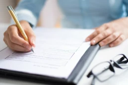 dłonie osoby przygotowującej dokumentację środowiskową firmy; obok czarne okulary